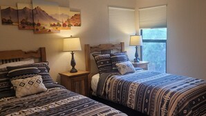 Una camera da letto con due letti, ognuno con biancheria e cuscini decorati. Sono presenti due comodini con lampade e una finestra con persiane.