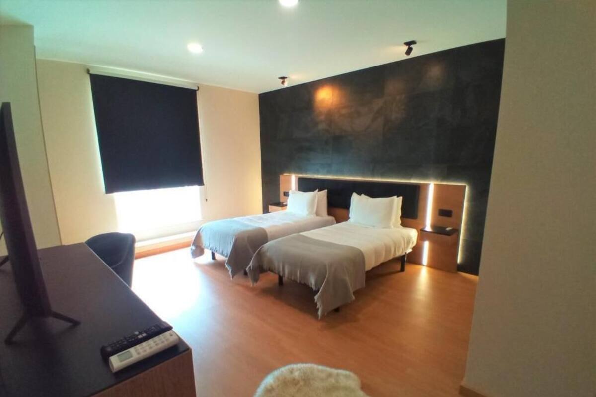 A modern hotel room with a large bed, a desk with a computer, and a large window.