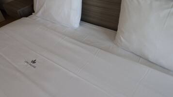 Una cama bien tendida con sábanas y almohadas blancas, un cabecero de madera y un logotipo en la colcha.