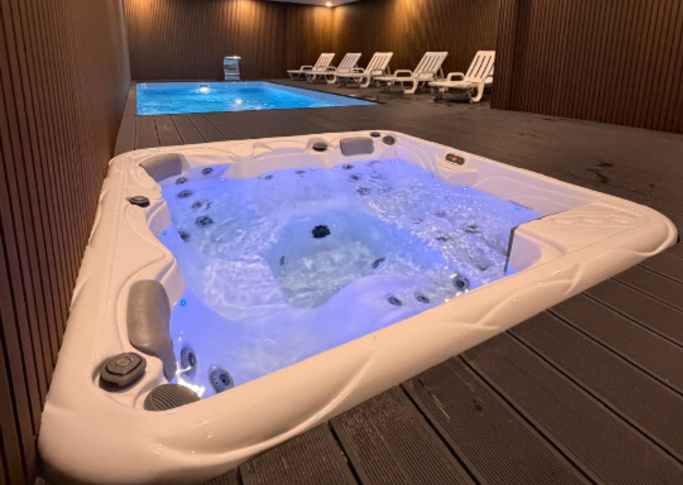 A hot tub with jets, surrounded by lounge chairs and a pool.