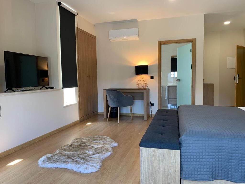 A modern bedroom with a bed, a desk, a chair, and a television.