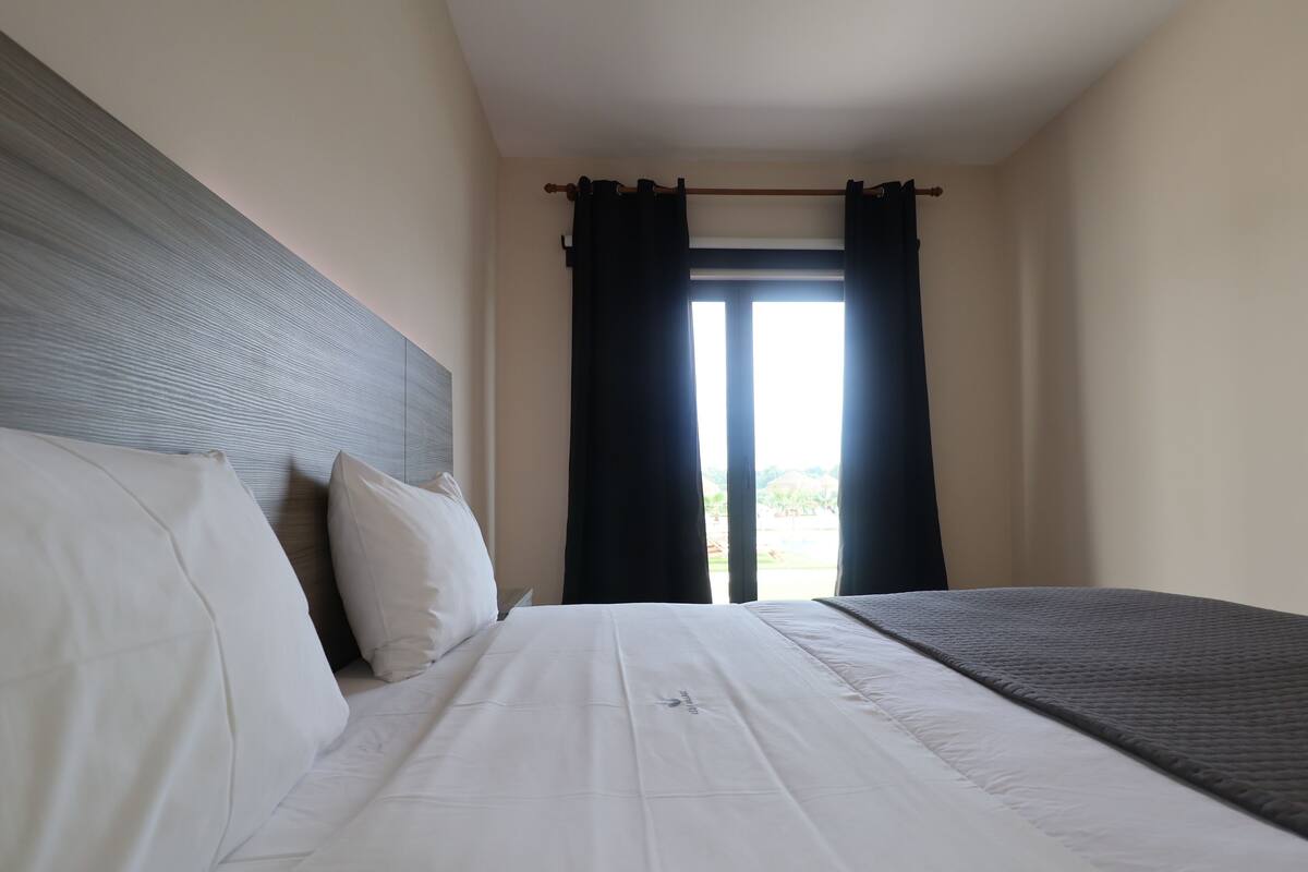 A hotel room with a bed, a headboard, and a window with curtains.
