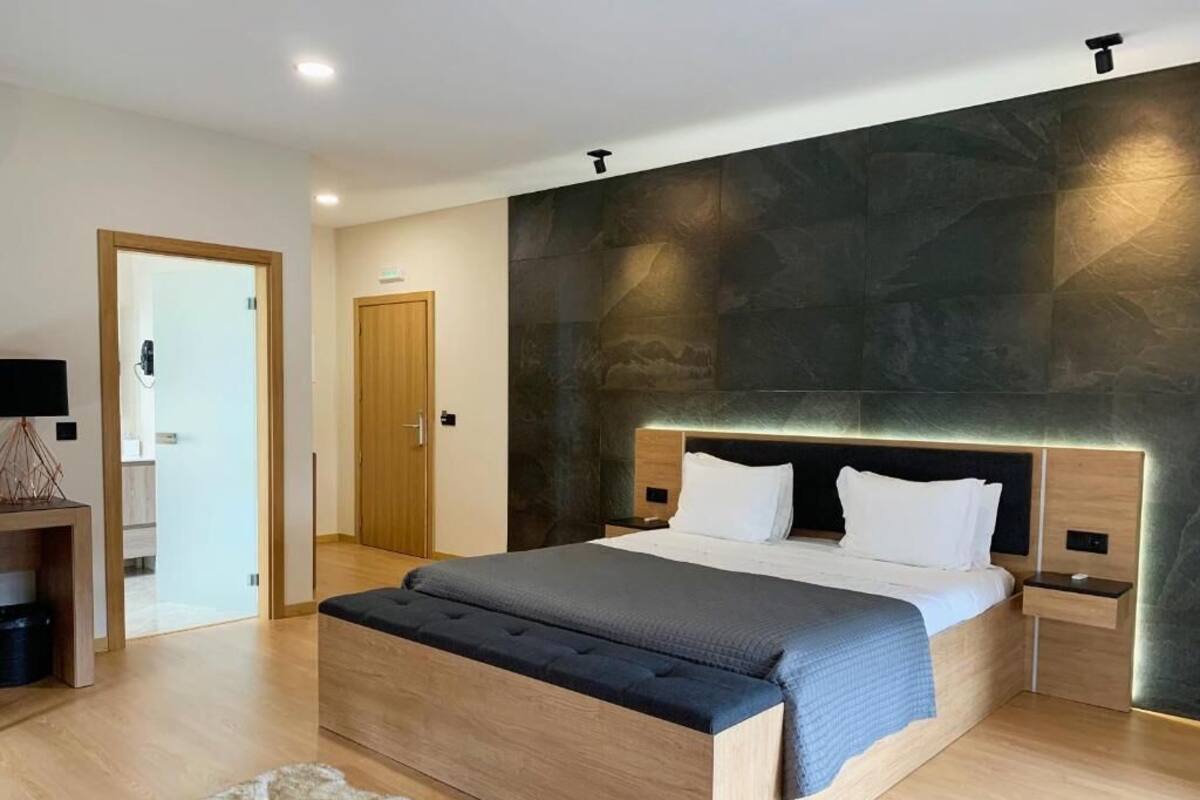 A modern bedroom with a large bed, wooden headboard, bedside tables, and a stone accent wall.