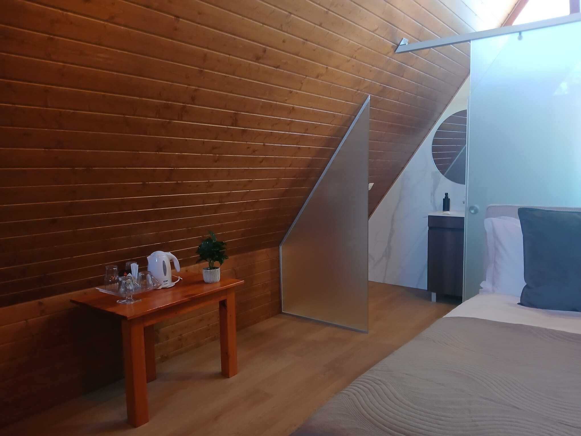 Une pièce aux murs en bois, avec un lit, une petite table sur laquelle se trouvent une bouilloire et une plante, et une cloison en verre.