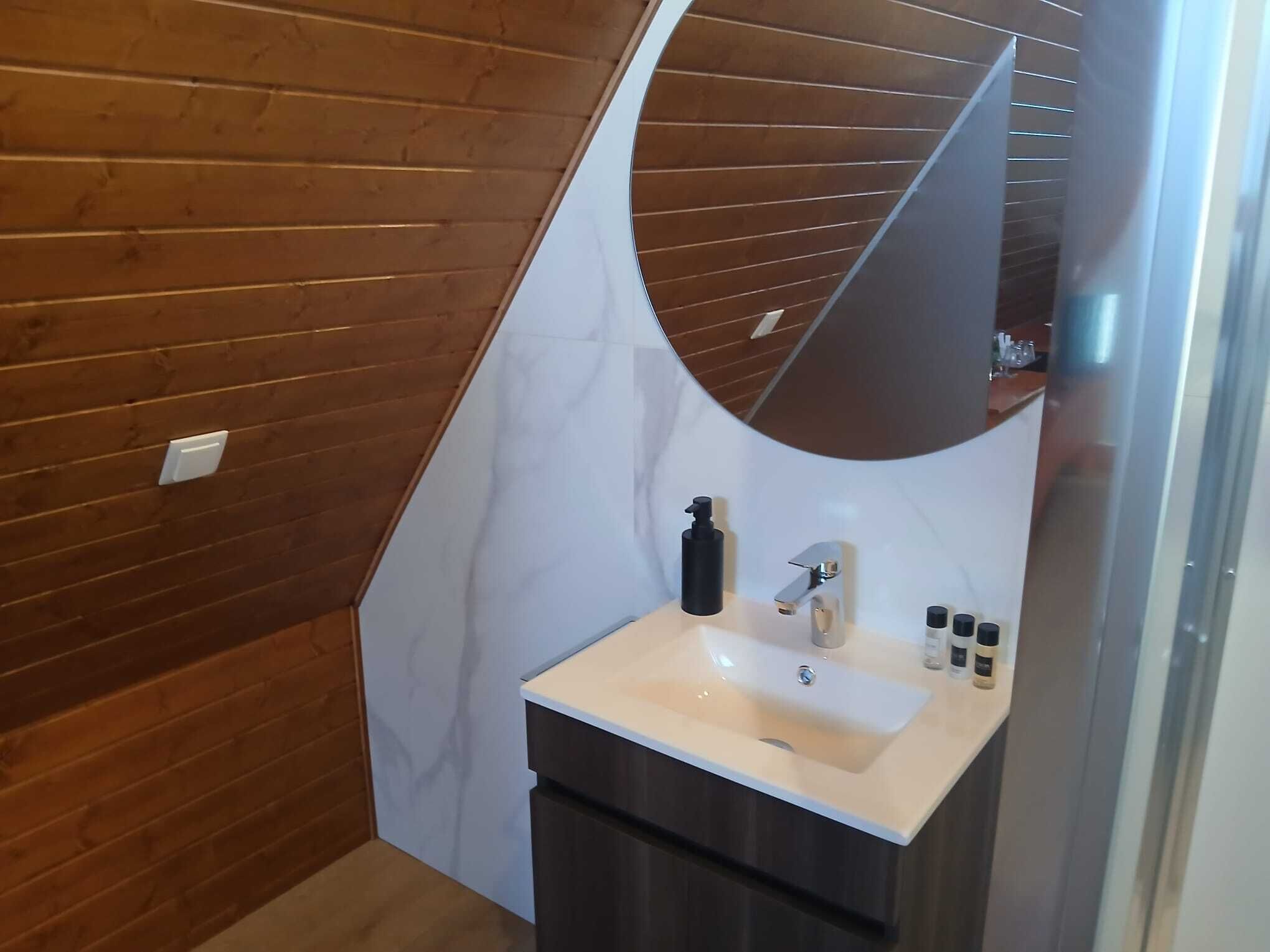 Une salle de bain avec un mur en bois, un lavabo blanc, un miroir et un meuble sombre.