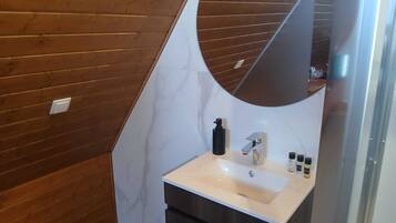 A bathroom with a wooden wall, a white sink, a mirror, and a dark cabinet.