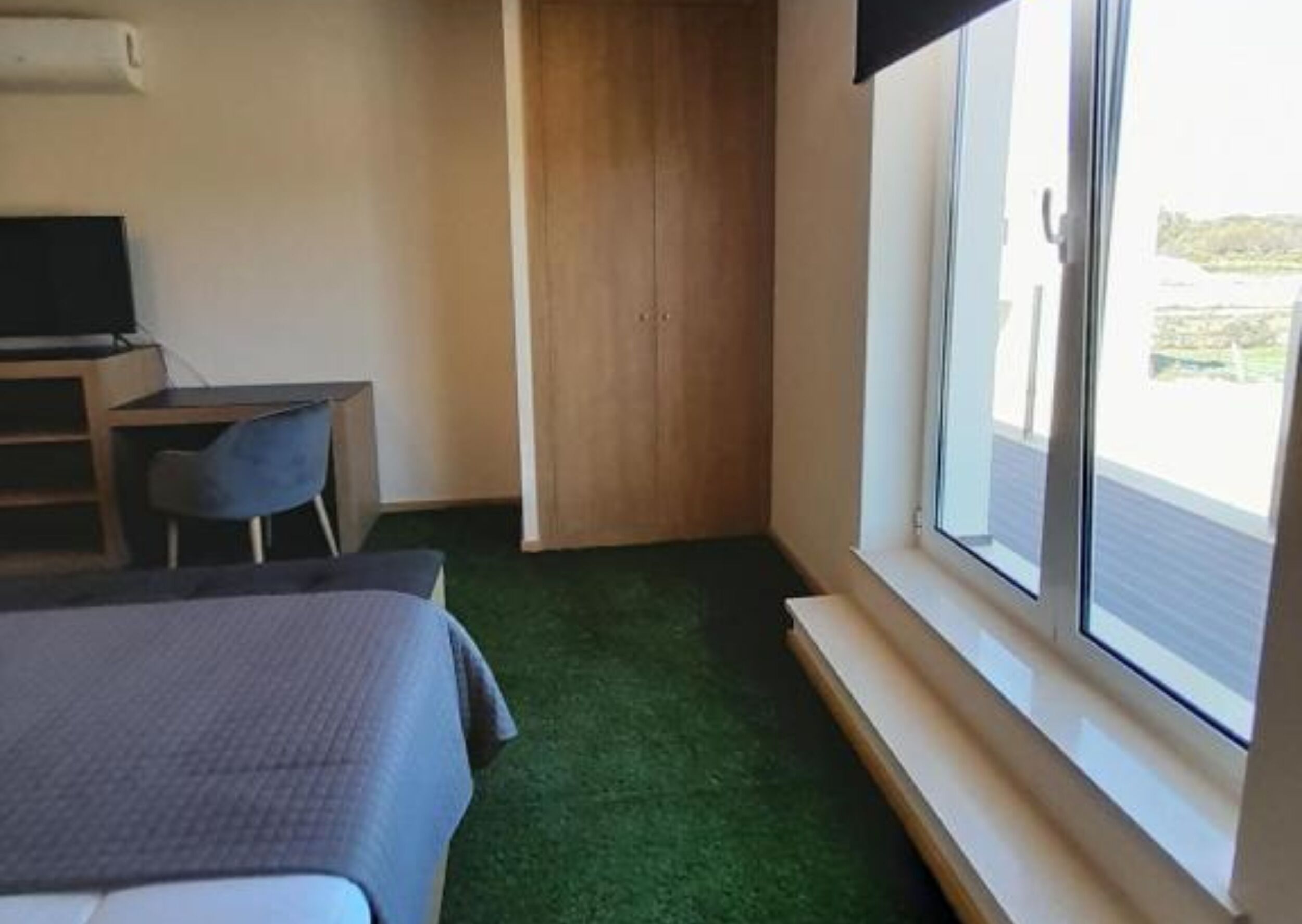 A hotel room with a bed, a desk, a chair, a television, and a window with a view of the outdoors.