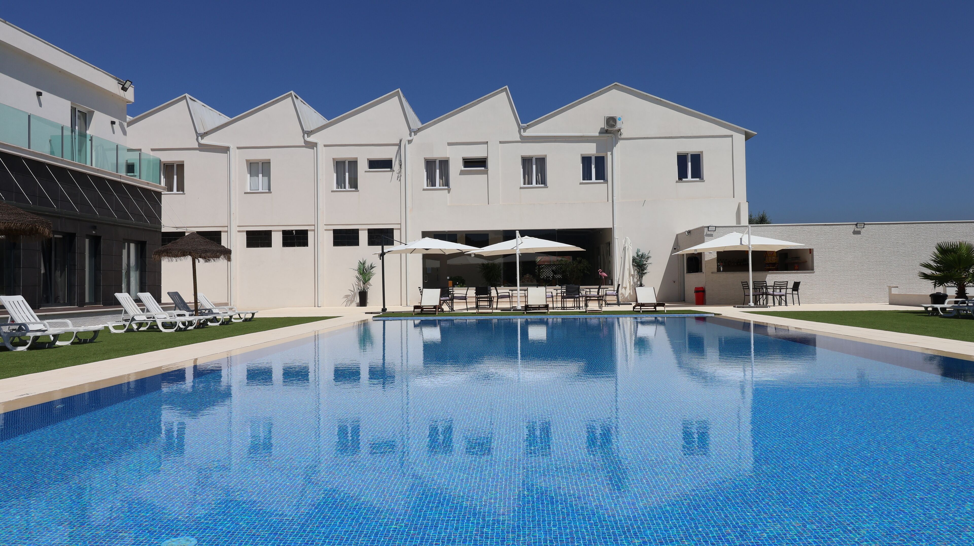 Un hôtel moderne doté d’une piscine, de chaises longues et d’un espace extérieur aménagé pour se détendre.
