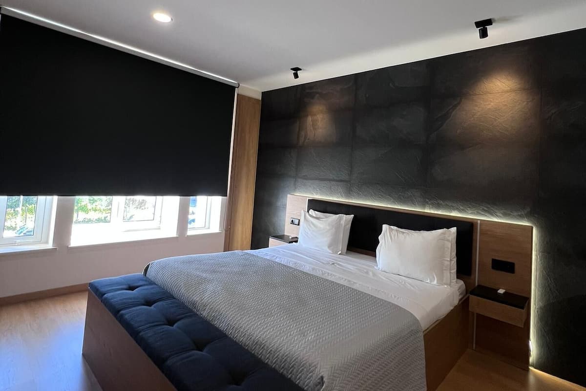 A modern bedroom with a large bed, a bench, a nightstand, and a window with a view.