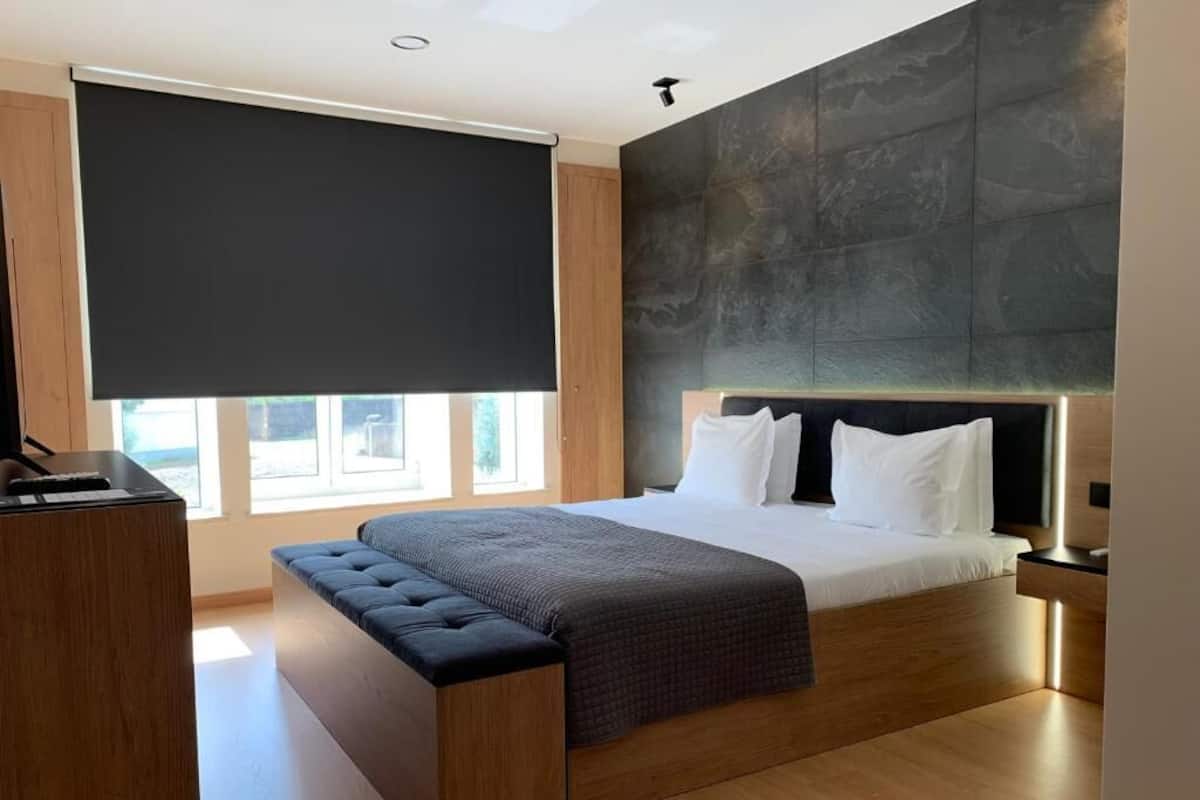 A modern bedroom with a large bed, a bench, a desk, and a large window with a view.