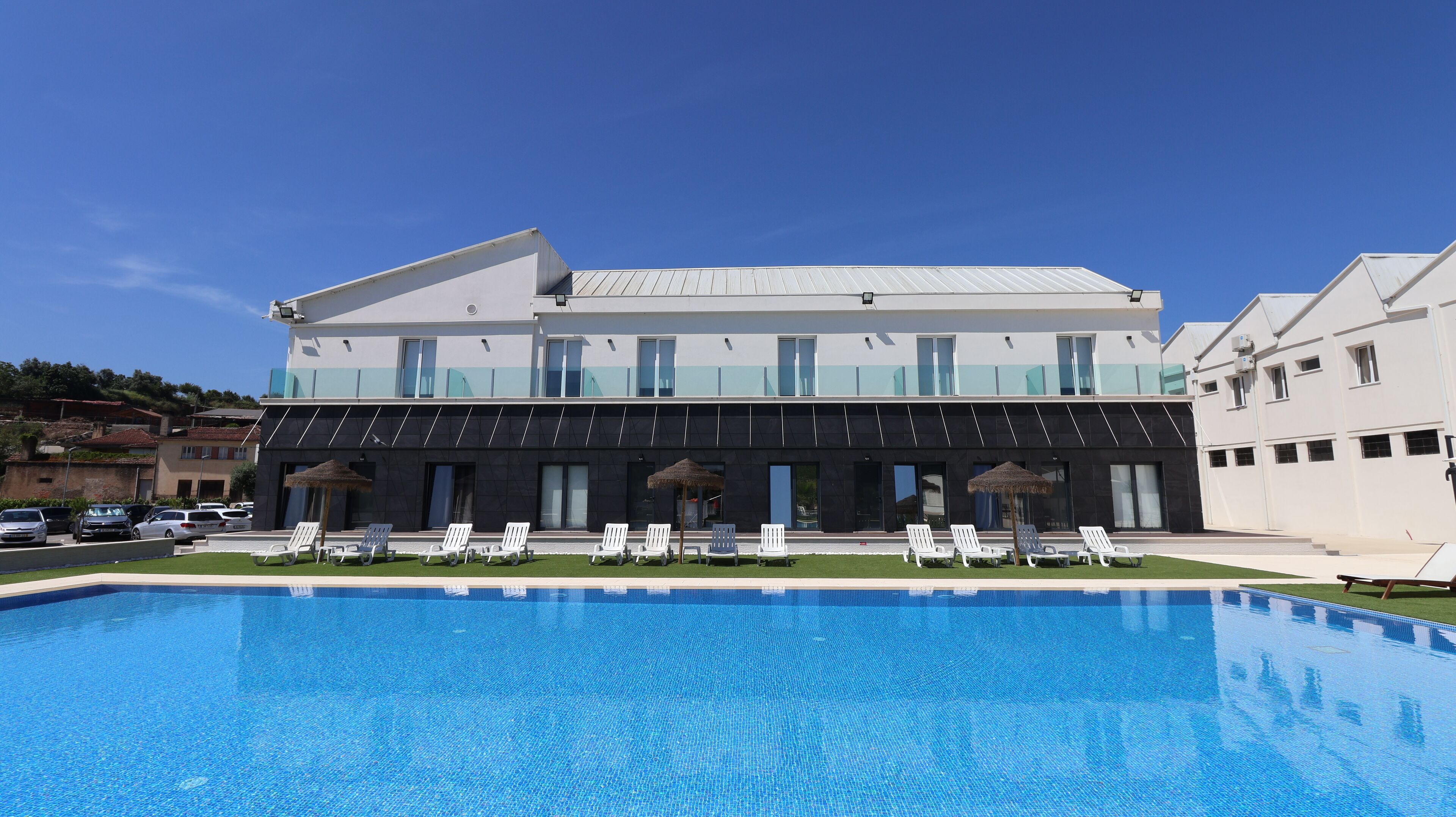 A modern hotel with a swimming pool, multiple balconies, and outdoor seating areas.