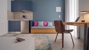 Una habitación moderna con kitchenette, un sofá con cojines coloridos, un escritorio de madera y una silla.