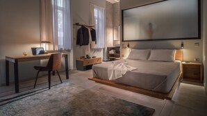 Un dormitorio moderno con una cama grande, un escritorio, y una silla. Hay un armario, un espejo, y una mesita de noche con una lámpara.
