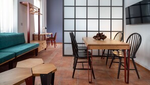 Una sala de estar moderna con un sofá, una mesa de comedor con sillas, un televisor montado en la pared y un ventanal con diseño de cuadrícula.