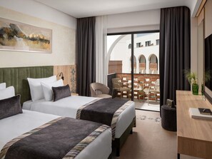 Hotellihuone, jossa on kaksi sänkyä, työpöytä, tuoli ja parveke, jolta on näkymä rakennuksiin.