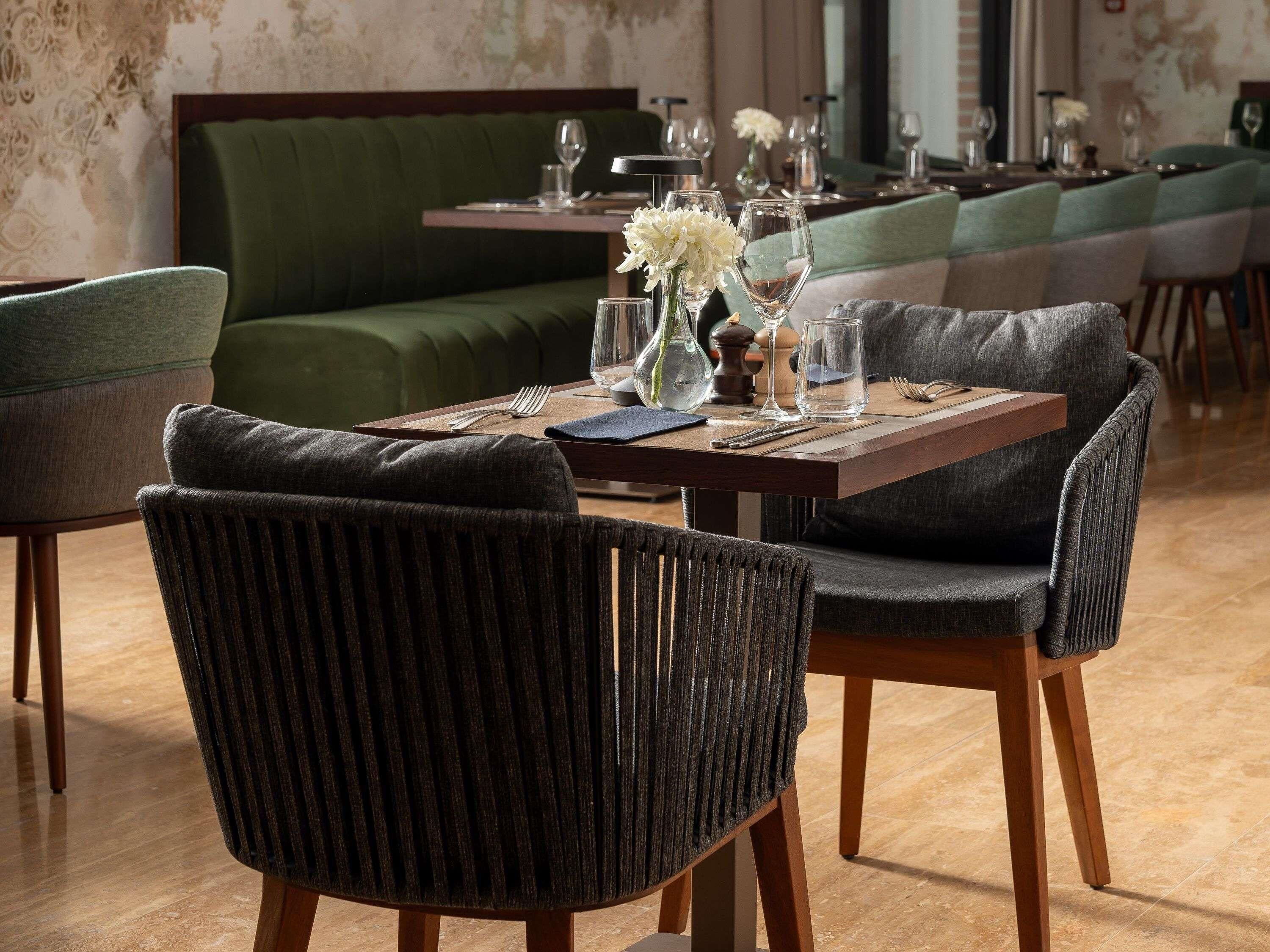 A restaurant with a green sofa, dining tables set with glassware, and striped chairs.