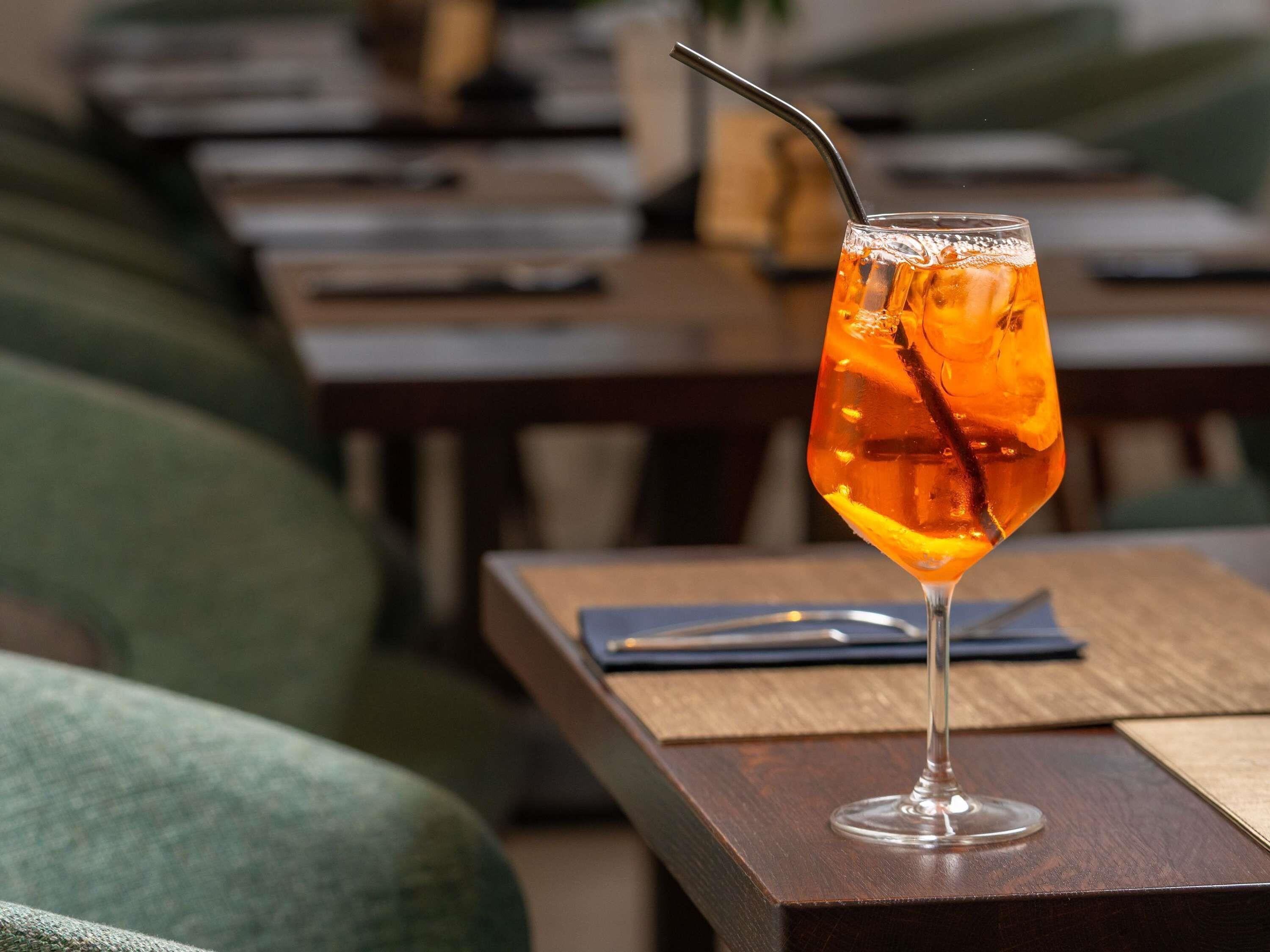 Un verre d’une boisson ambrée, avec une paille, posé sur une table en bois dans un restaurant.