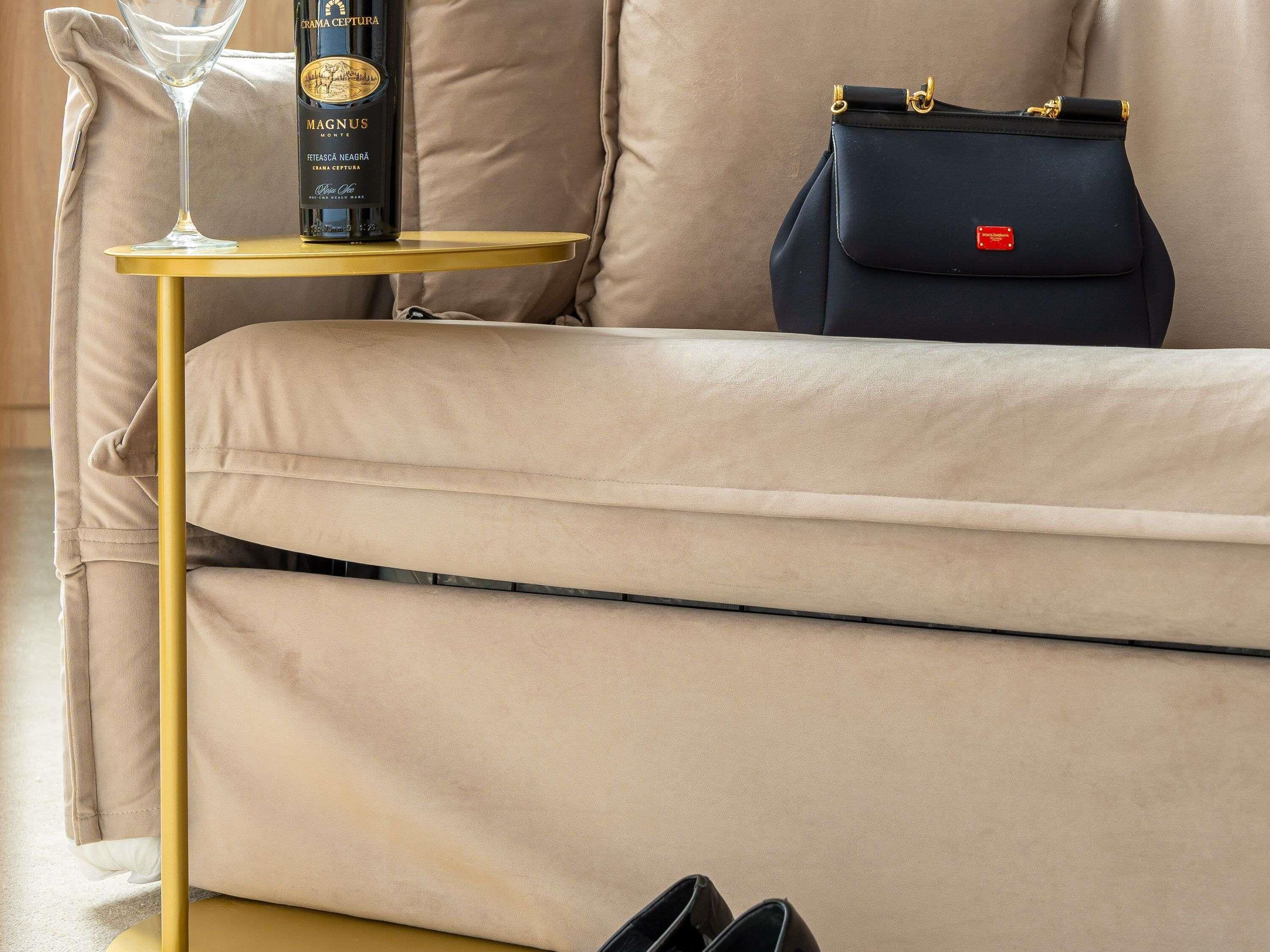A beige sofa with a gold frame, a black handbag, a bottle of wine, and a pair of black shoes on the floor.