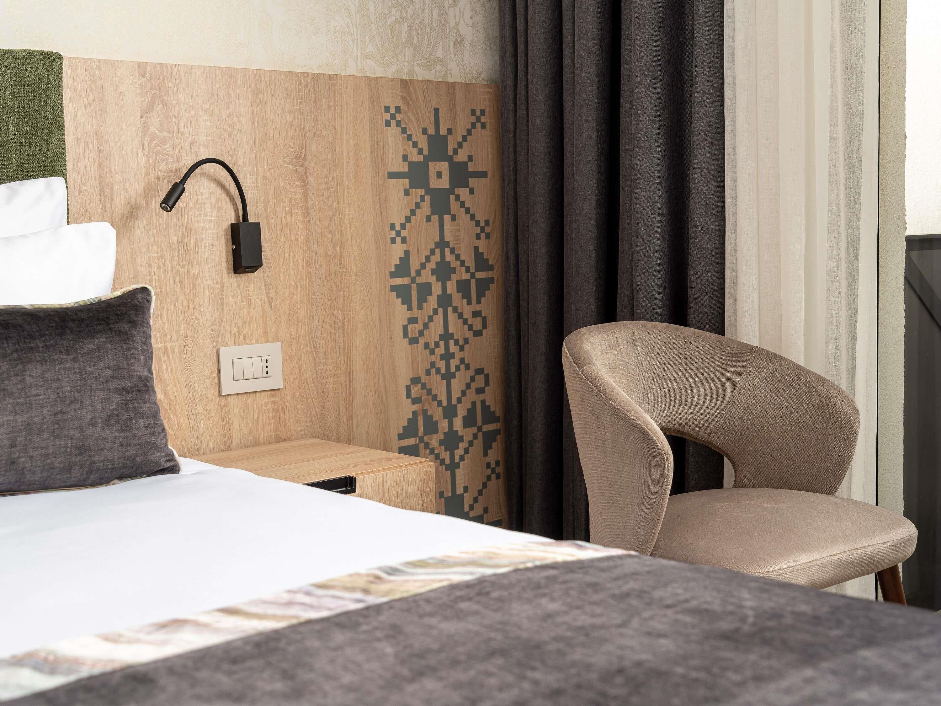 Habitación de hotel con cama, mesita de noche, lámpara, silla y pared con diseño.