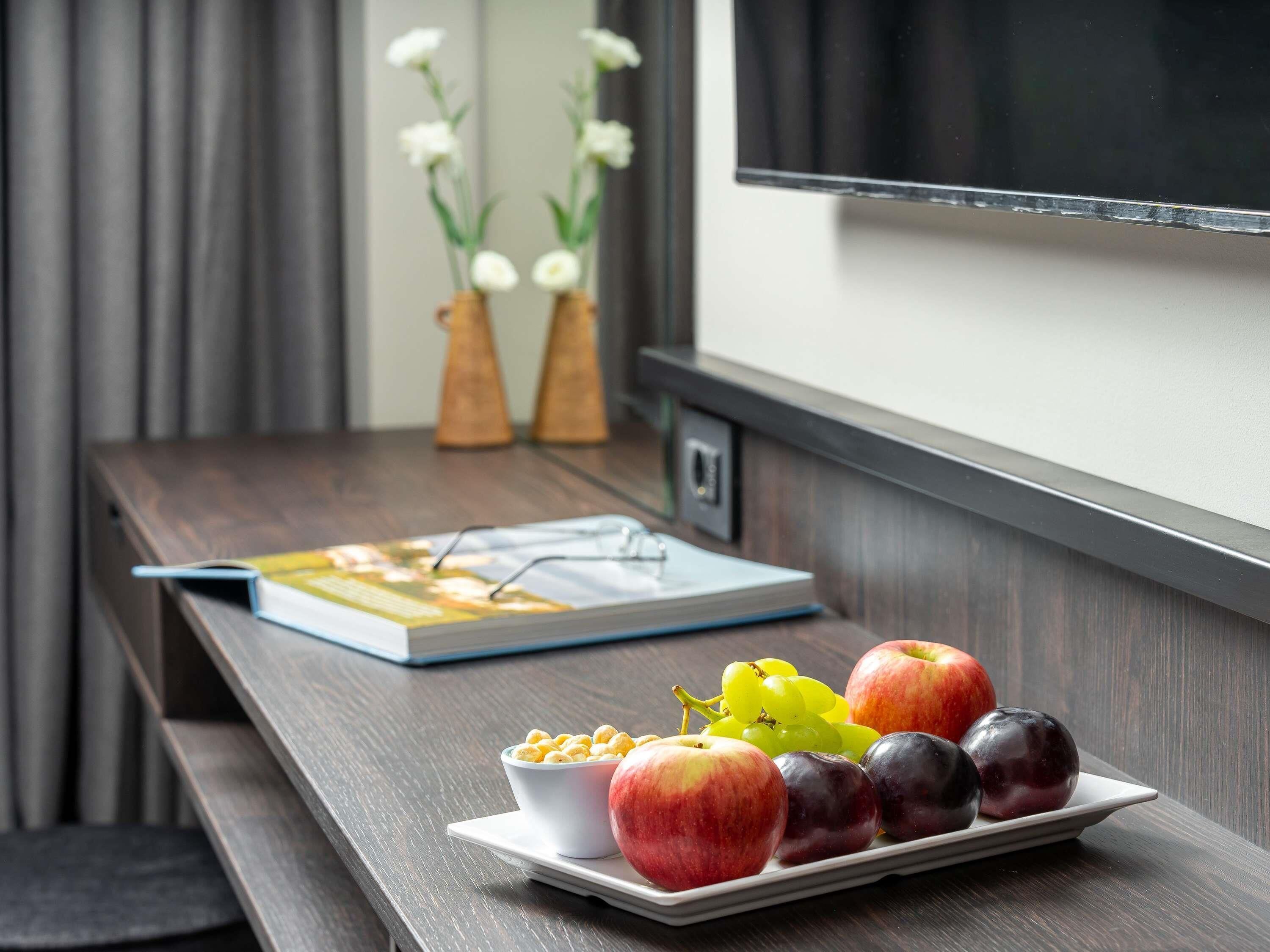 A wooden table with a plate of fruits, a bowl of cereal, and a book.