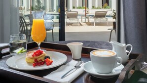 A breakfast tray with pancakes, fruit, and coffee on a balcony overlooking a pool and outdoor seating area. - Mercure Conacul Cozieni (Ganeasa)
