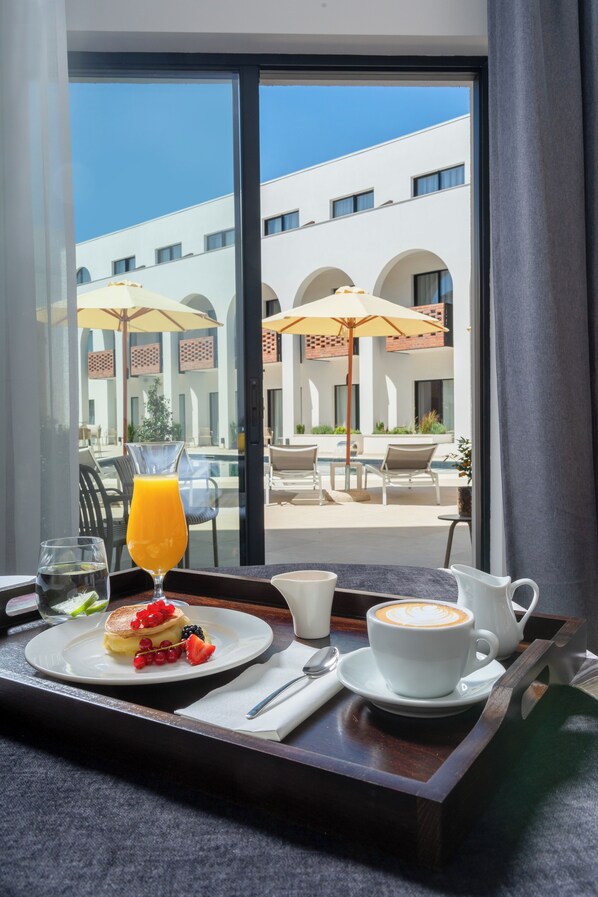 Bandeja de desayuno con panqueques, fruta y café en un balcón con vista a una piscina y zona de estar exterior.