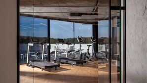 A gym with exercise equipment, large windows, and a view of the outdoors. - Mercure Conacul Cozieni (Ganeasa)