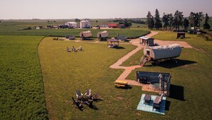 An aerial view of a farm with a large barn, covered wagons, and a picnic area with chairs and a table.