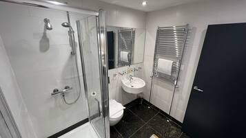 A modern bathroom with a glass-enclosed shower, a white sink, and a toilet.