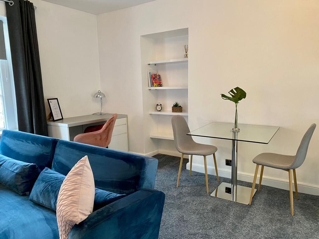 Una sala de estar moderna con un sofá azul, una mesa de vidrio y dos sillas.