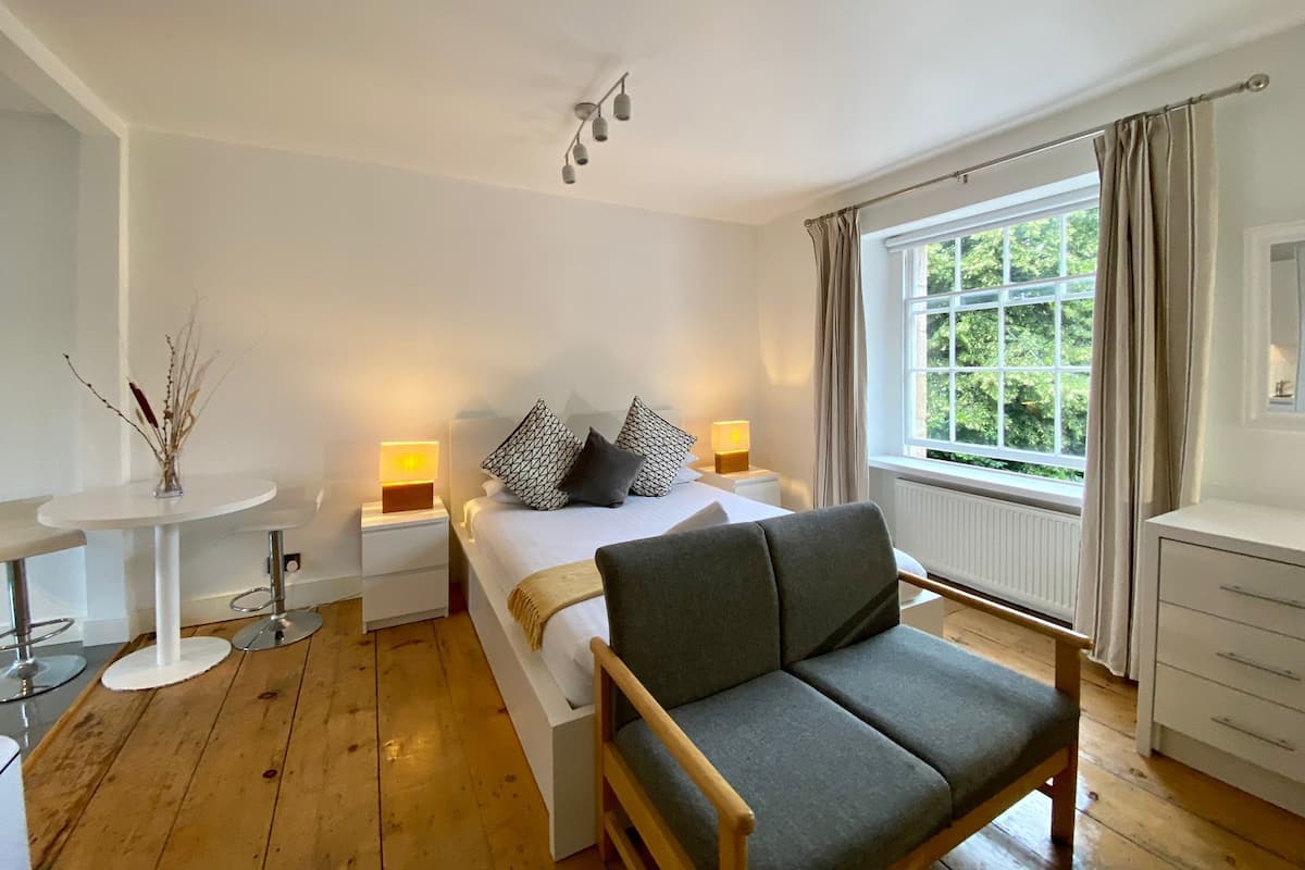 A bedroom with a bed, bedside lamps, a chair, a small table, and a window with curtains.