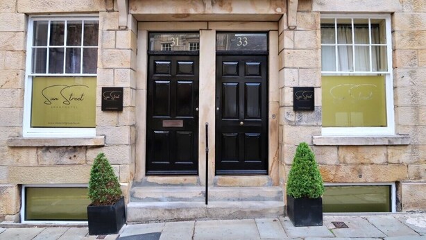 A building with two black doors labeled 31 and 33, a stone facade, and two potted plants on the steps. - Sun Street ApartHotel (Lancaster)