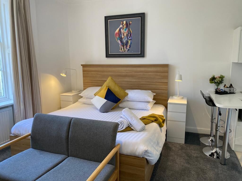 Een hotelkamer met een bed, een bureau, een stoel, een nachtkastje en een lijst met een foto aan de muur.