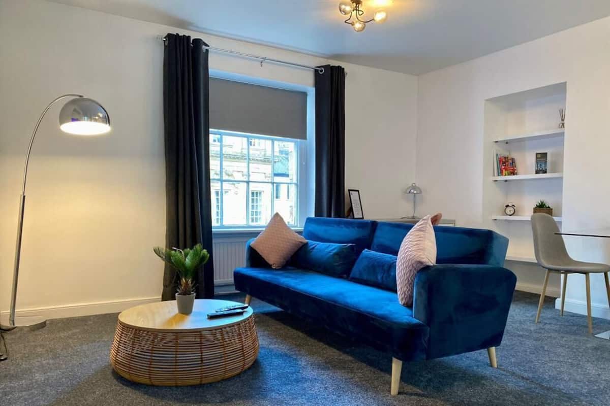 A modern living room with a blue sofa, a round coffee table, a floor lamp, and a bookshelf.