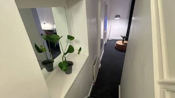 Una escalera con alfombra oscura, paredes blancas y un pequeño ventanal con una planta en maceta.