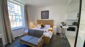 A modern hotel room with a bed, a sofa, a desk, and a window with curtains. - Sun Street ApartHotel (Lancaster)