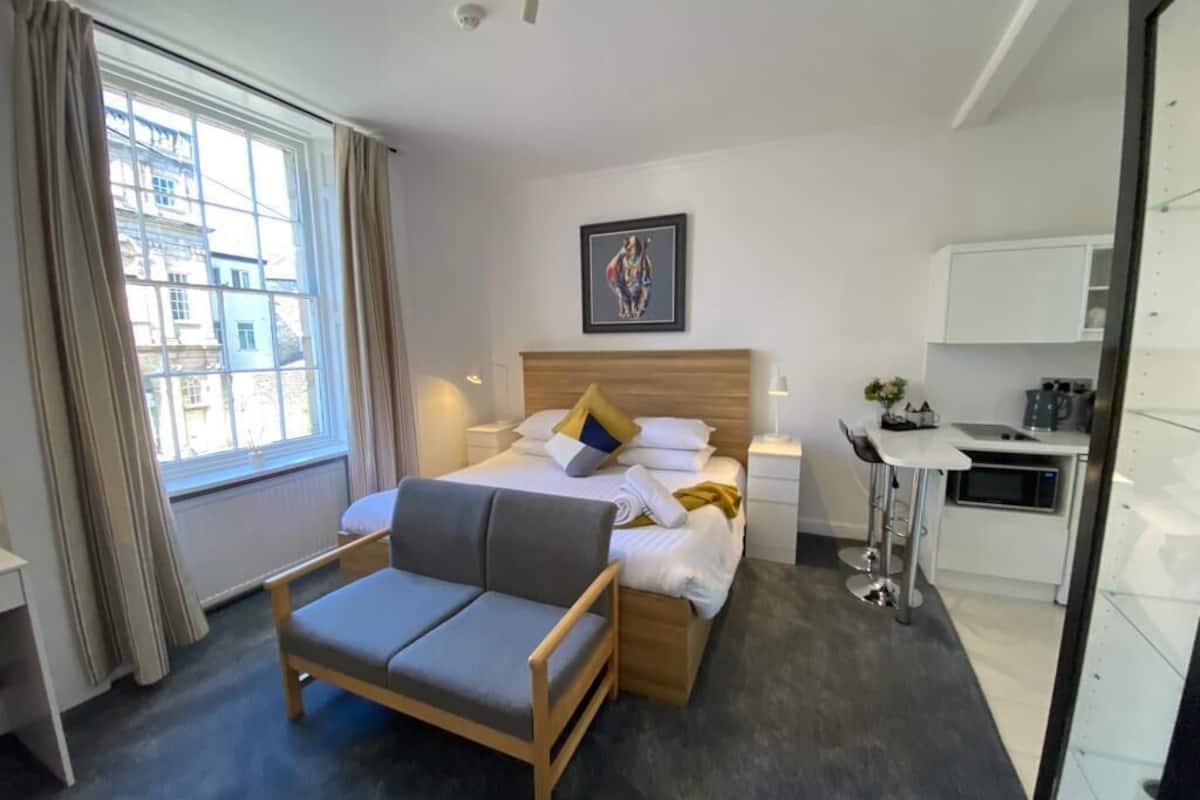 A modern hotel room with a bed, a sofa, a desk, and a window with curtains.