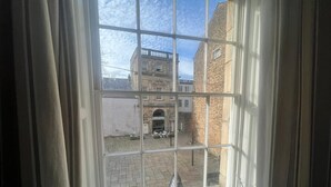 A window with a view of a courtyard, a building with a cross on it, and a small potted plant on the windowsill. - Sun Street ApartHotel (Lancaster)