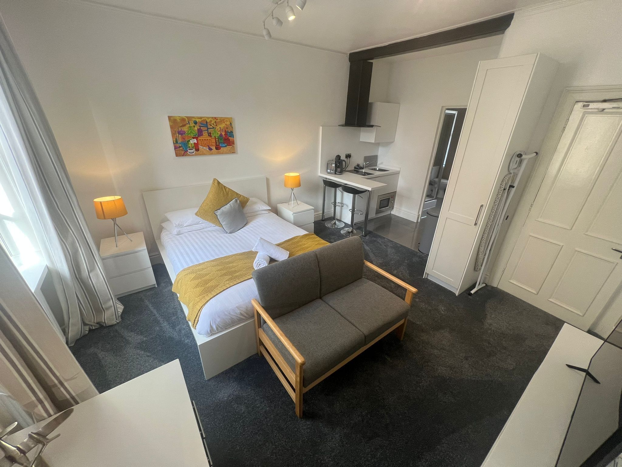 A modern hotel room with a bed, a sofa, a desk, and a kitchenette.