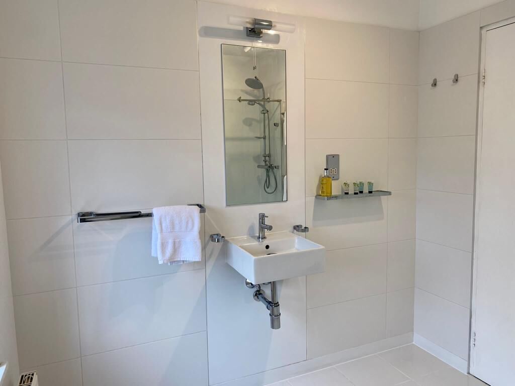 Ein modernes Badezimmer mit einer gläsernen Duschkabine, einem weißen Waschbecken und einem Handtuchhalter.