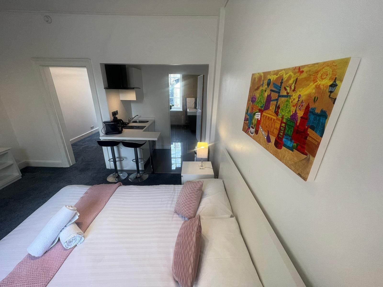 Una camera d'albergo con un letto, una scrivania, una sedia, una lampada e un quadro colorato appeso al muro.