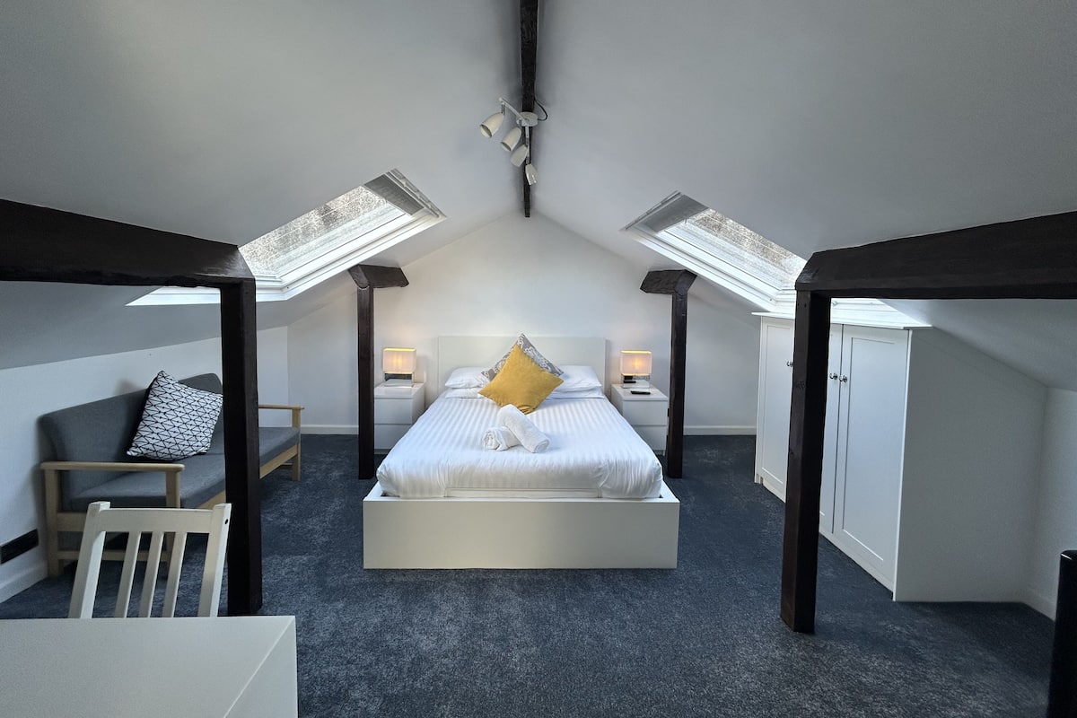 A bedroom with a skylight, a bed, bedside tables, a chair, and a wardrobe.