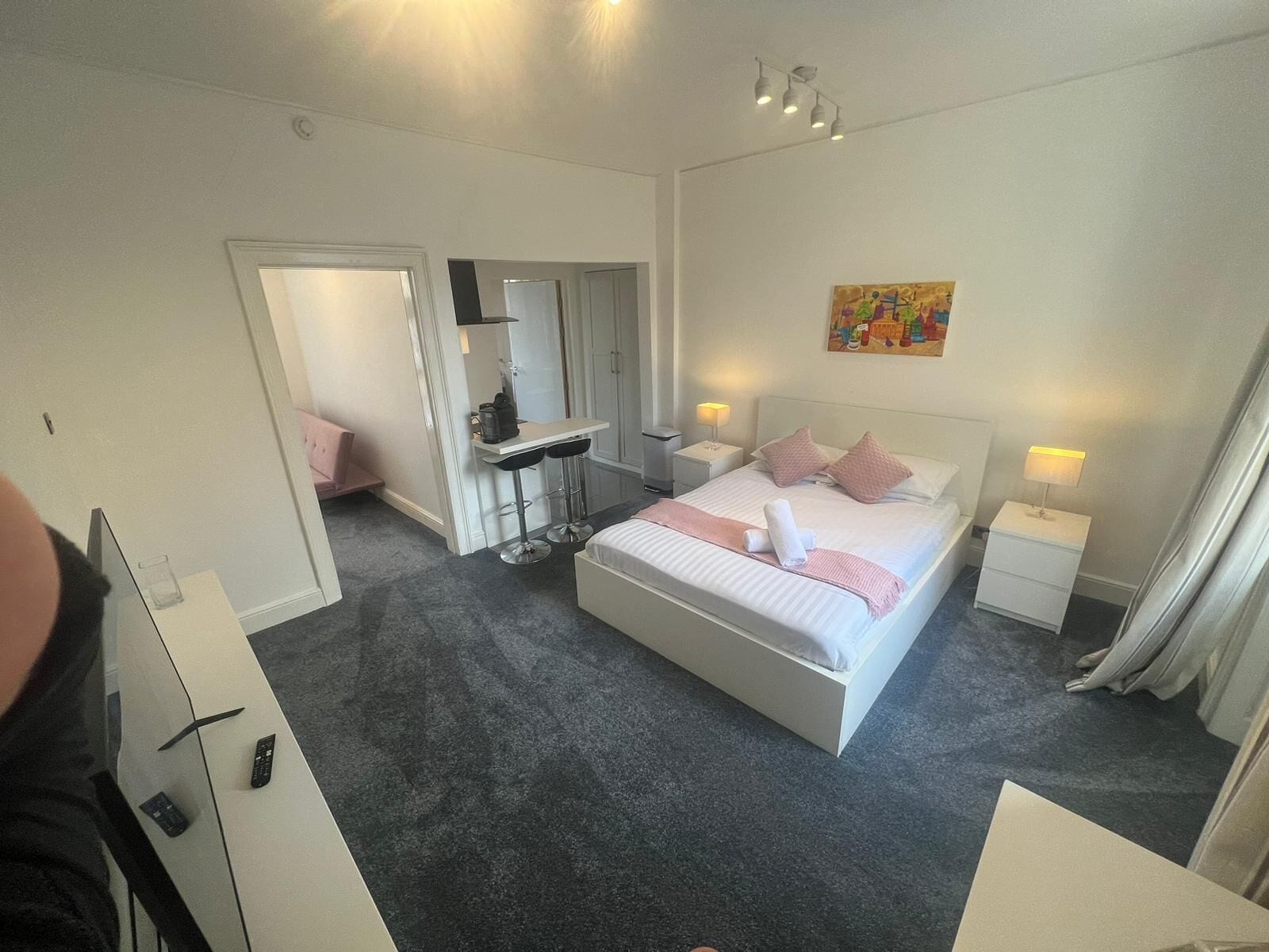 Habitación de hotel con cama, mesitas de noche, escritorio con silla, espejo y un cuadro en la pared.