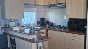 Cocina compacta con armarios de madera, estufa a gas, microondas y cafetera.