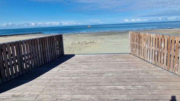 Un malecón de madera que conduce a una playa, con vista clara al océano y un barco a lo lejos.