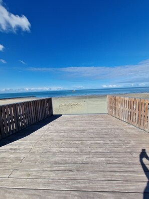 A wooden boardwalk leading to a beach with a clear view of the ocean and a distant boat.