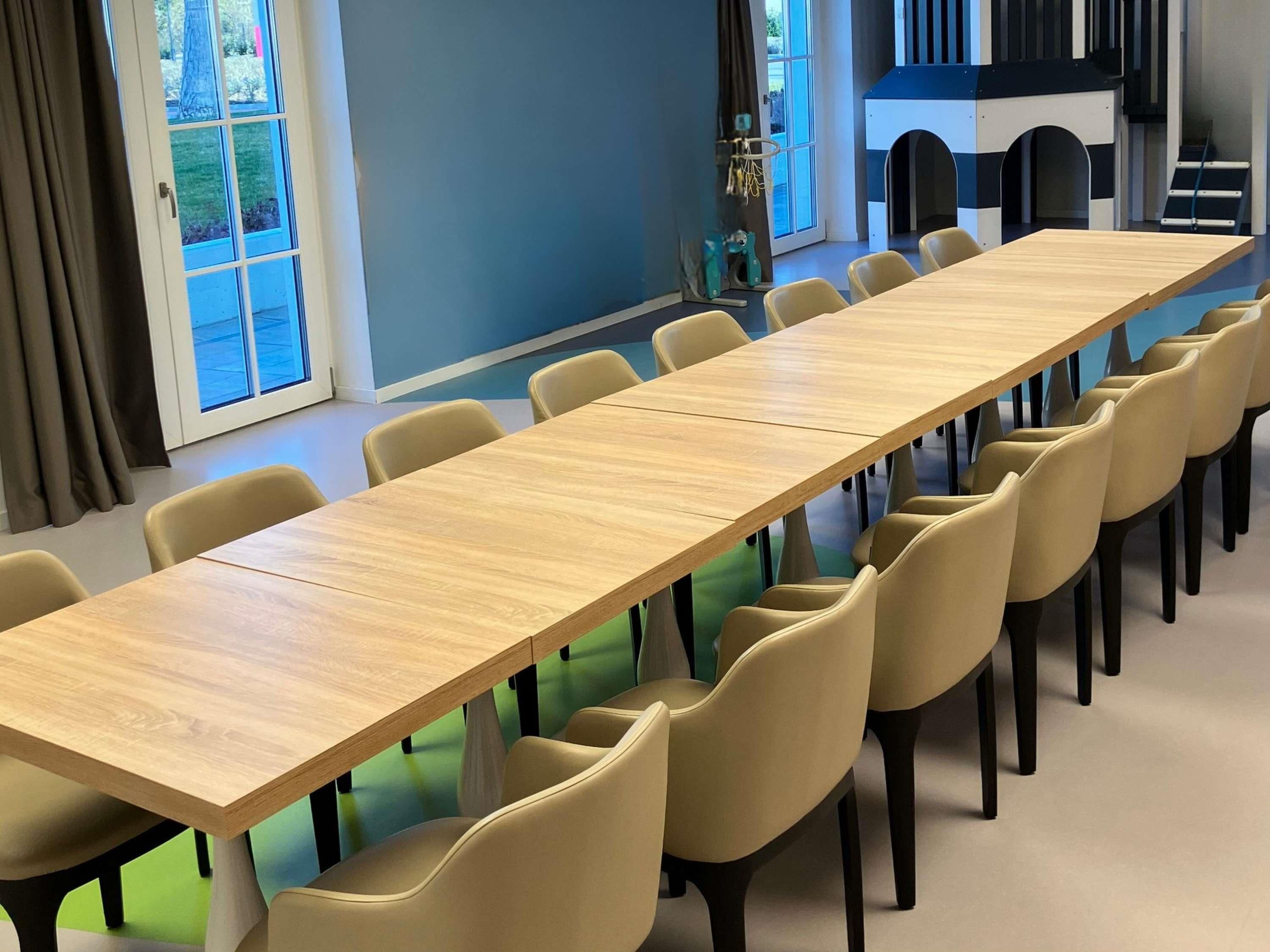 A conference room with a long table and chairs, a play area with a slide, and a view of the outdoors through large windows.