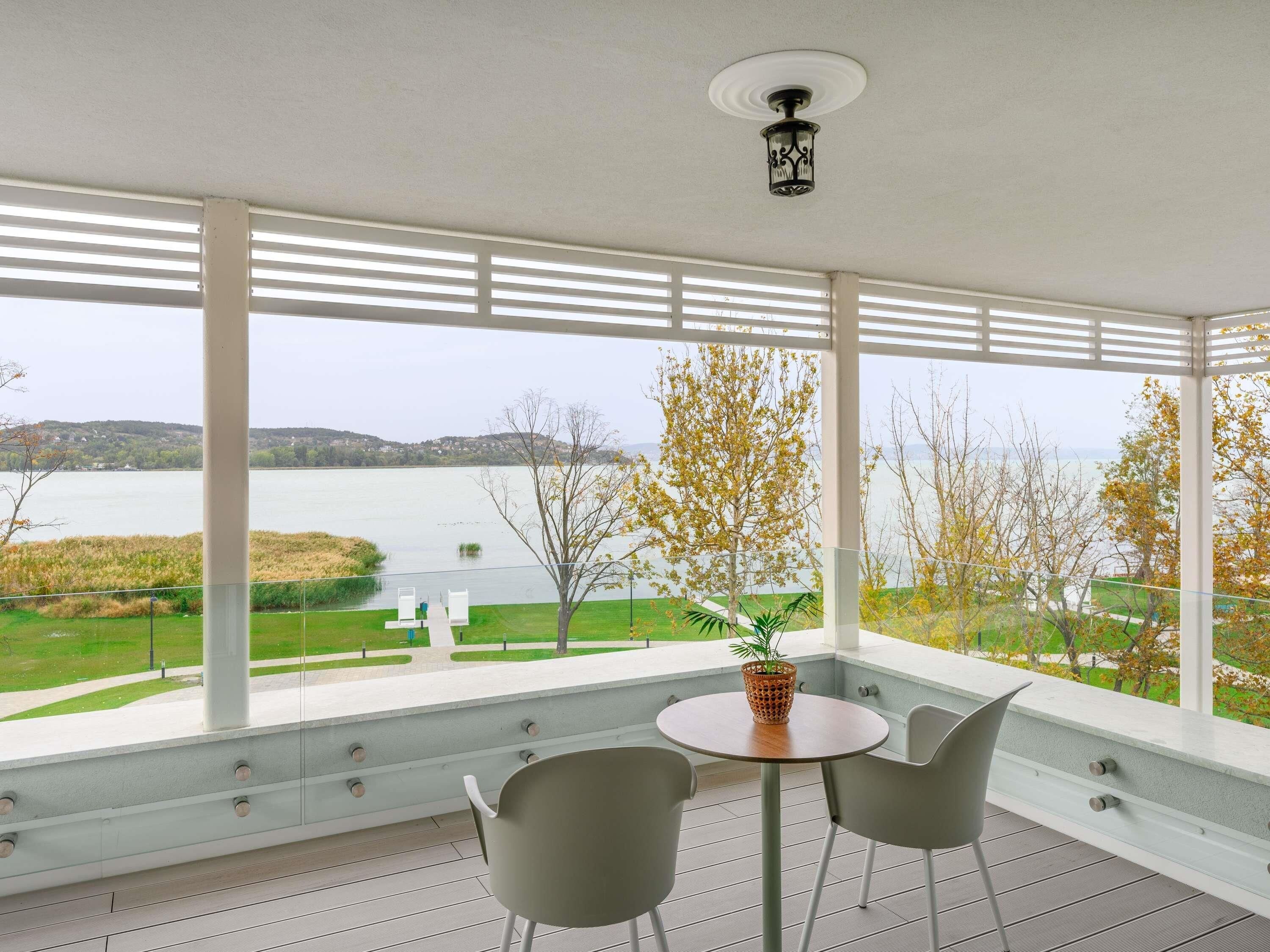 A balcony with a table and chairs, overlooking a lake and trees.