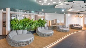 A modern lobby with circular seating areas, a green plant wall, and a ceiling with unique light fixtures. - Mövenpick Balaland Resort Lake Balaton (Szantod)