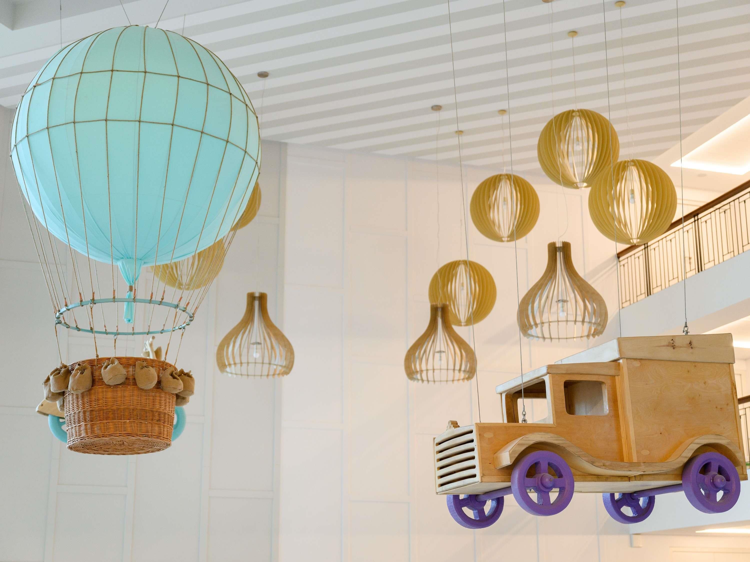 Una habitación con una cesta colgante, un coche de juguete de madera y varias lámparas colgantes.
